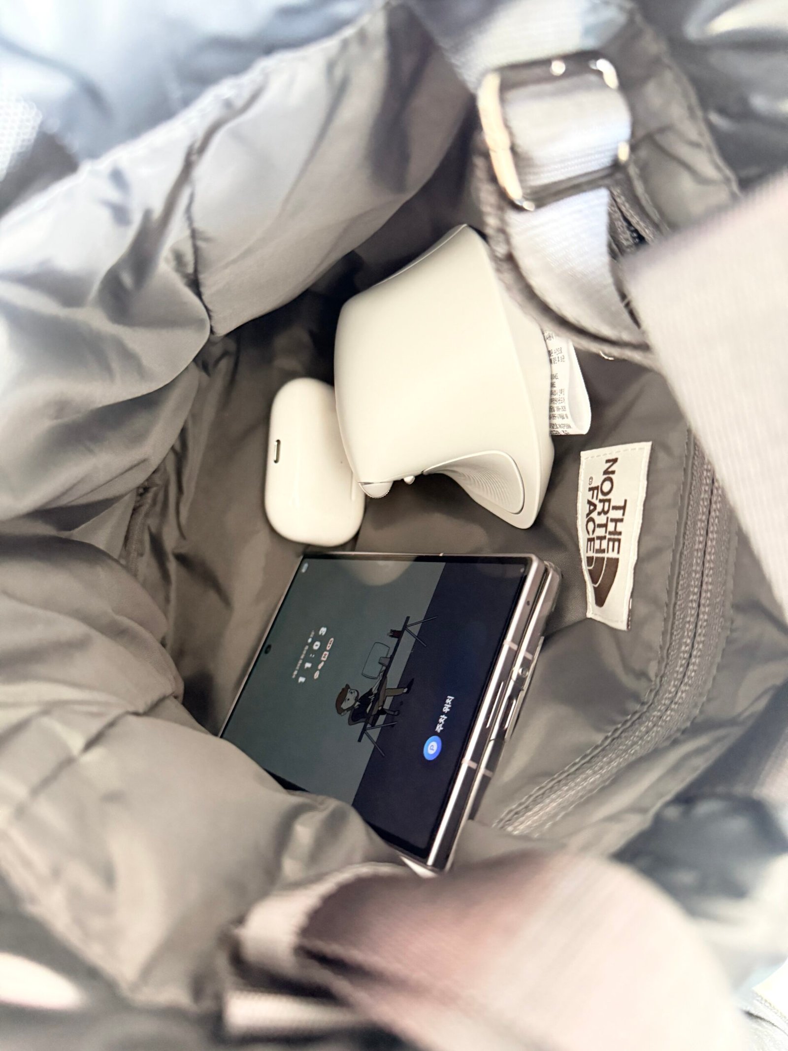 Phone and two white accessories placed inside the open Bonney mini bucket bag